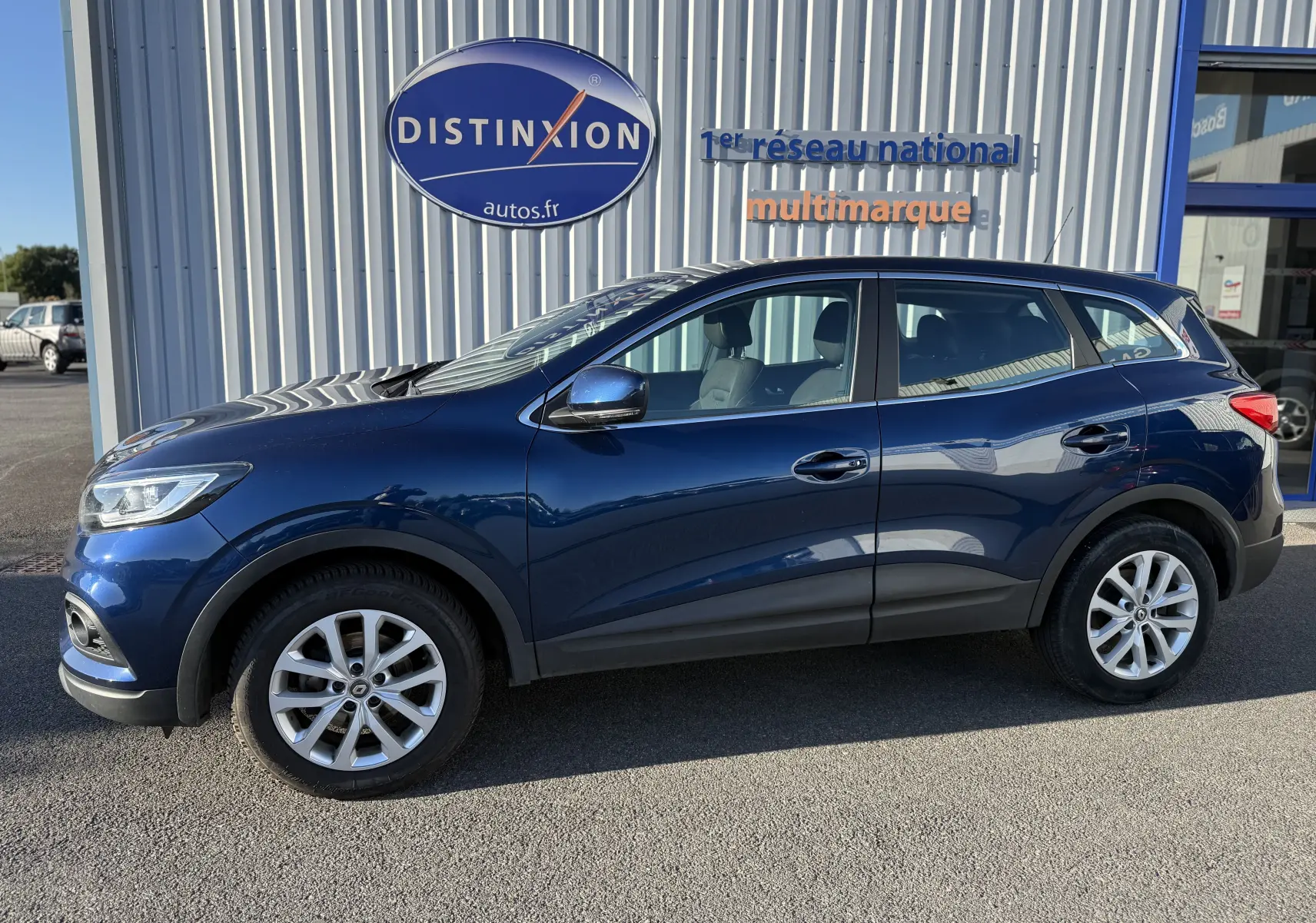 Profil côté gauche d'un Renault Kadjar bleu 2019, SUV compact avec jantes alliage et vitres teintées, stationné devant un bâtiment.