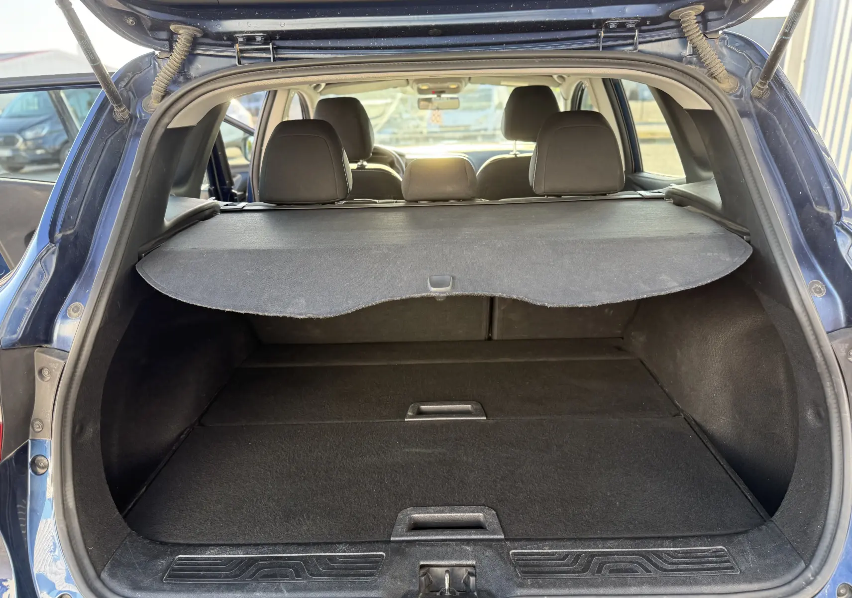 Vue arrière du coffre ouvert d'un Renault Kadjar bleu 2019, avec cache-bagages déployé et sièges arrière visibles.