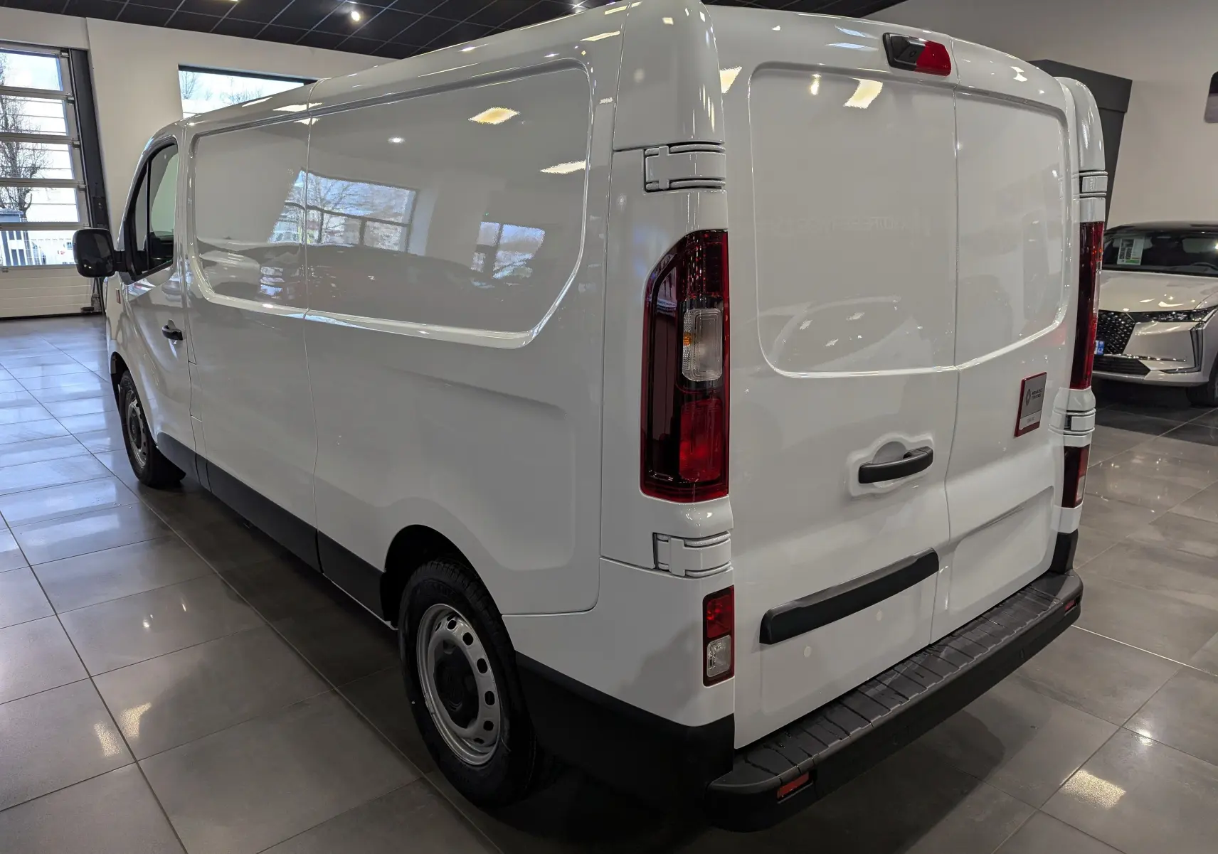 Vue 3/4 arrière droite du Renault Trafic Fourgon blanc minéral 2025 en intérieur, soulignant ses portes arrière et sa silhouette lisse.