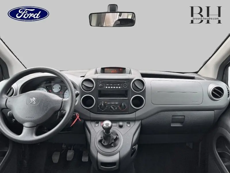 Vue frontale de l'intérieur du Peugeot Partner Tepee blanc Banquise, tableau de bord et volant avec levier de vitesse manuel visibles.