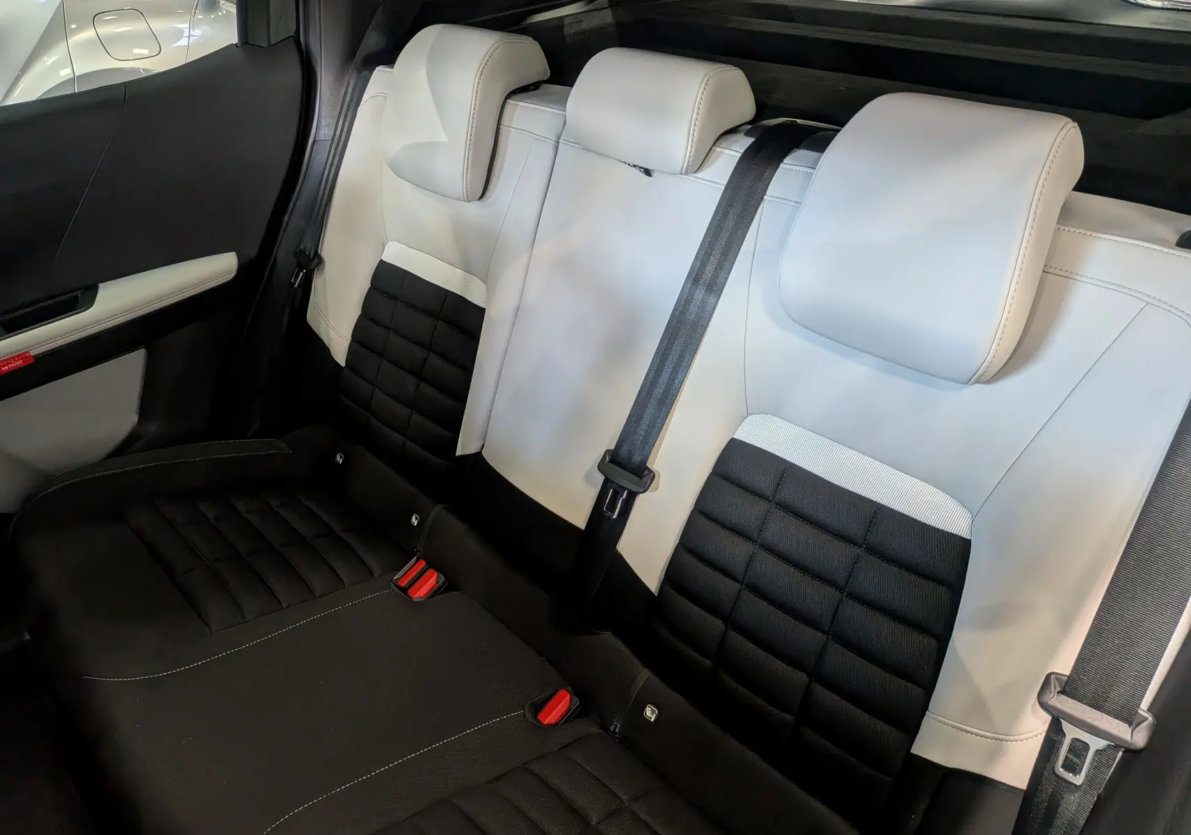 Vue intérieure arrière des sièges bicolores noir et blanc du Citroën C3 Aircross Hybride 2025 avec ceintures de sécurité visibles.
