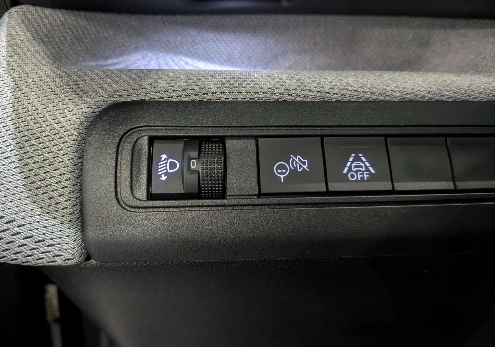 Gros plan sur les commandes d'assistance du tableau de bord d'une Citroën C3 Aircross Hybride 2025, tissu gris visible.