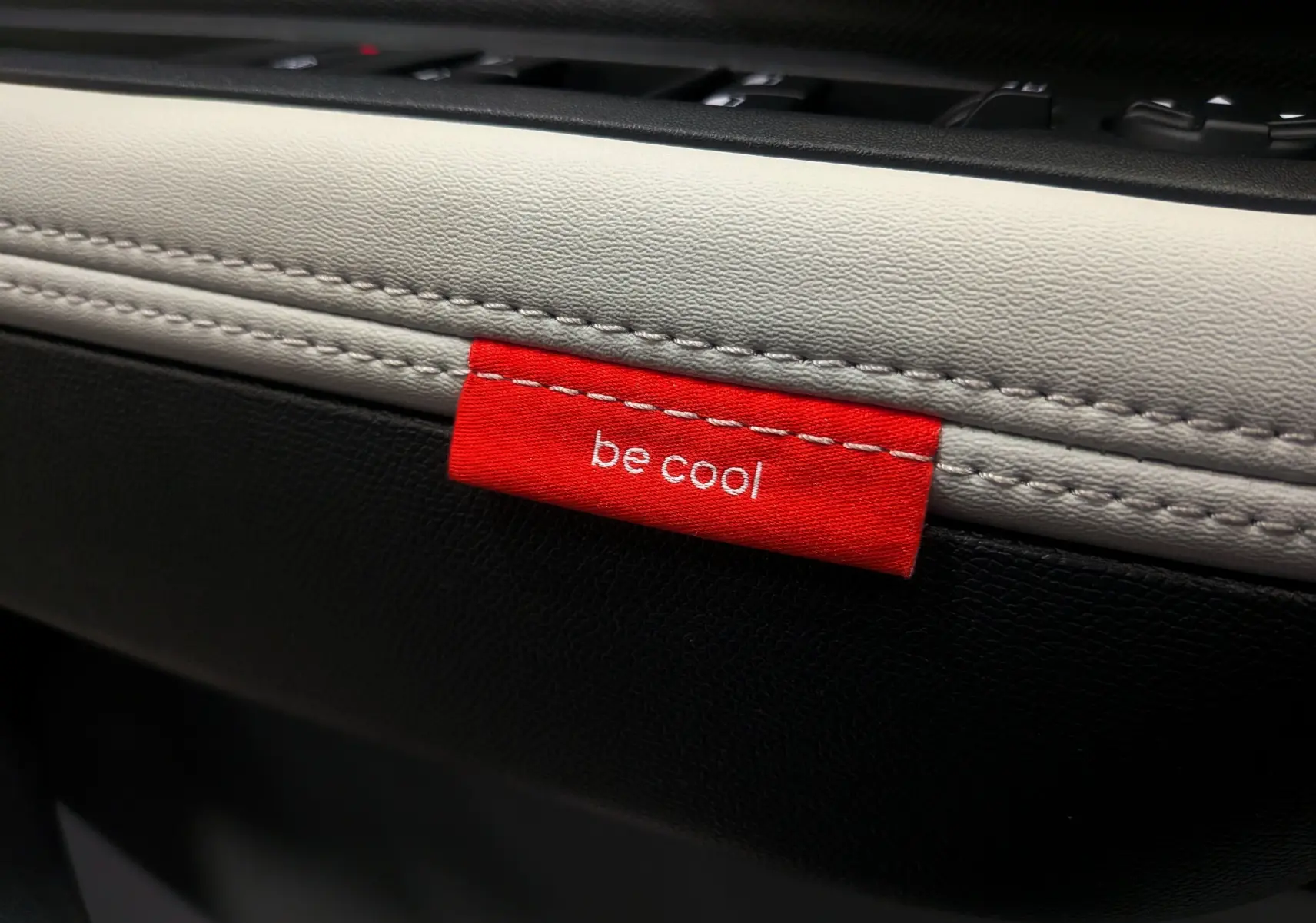 Détail intérieur montrant une étiquette rouge "be cool" sur la garniture bicolore noire et blanche d'une Citroën C3 Aircross Hybride 2025.