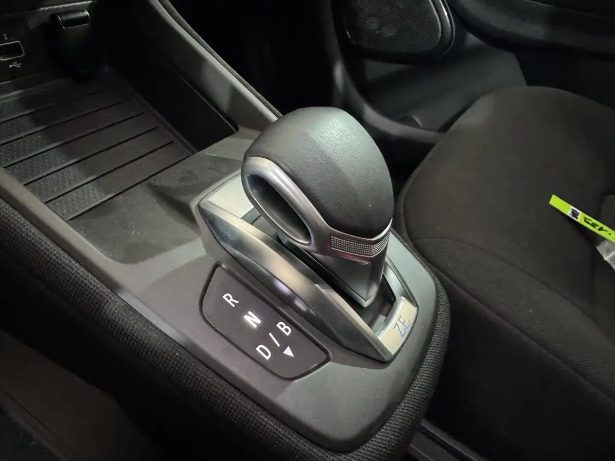 Gros plan sur le levier de vitesses automatique noir avec logo ZE dans l’habitacle de la Renault ZOE blanche.