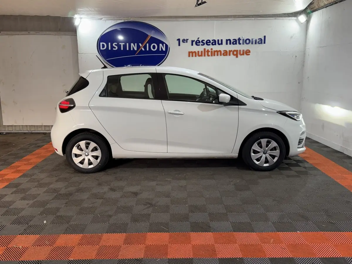 Renault ZOE Business 2020 blanc vue de profil côté gauche dans un garage avec sol noir et orange.
