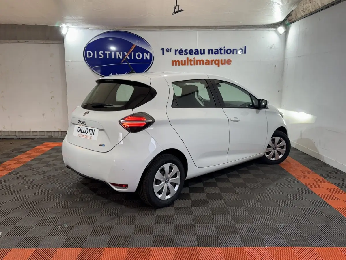 Renault ZOE blanche vue 3/4 arrière droit en intérieur, feux arrière LED et jantes acier avec enjoliveurs.