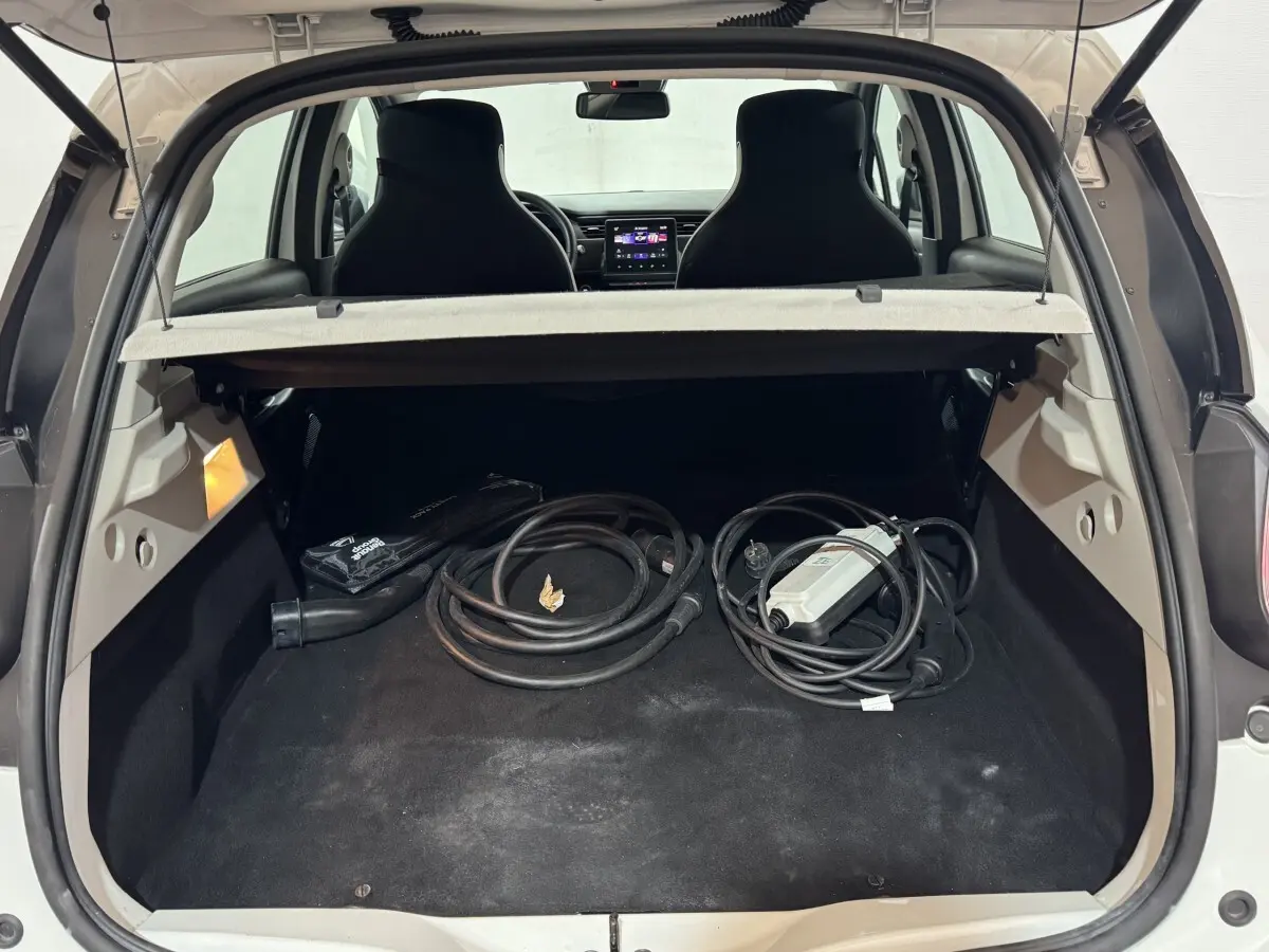 Coffre ouvert d’une Renault ZOE blanche vue de l’arrière, avec câbles de recharge électrique visibles à l’intérieur.