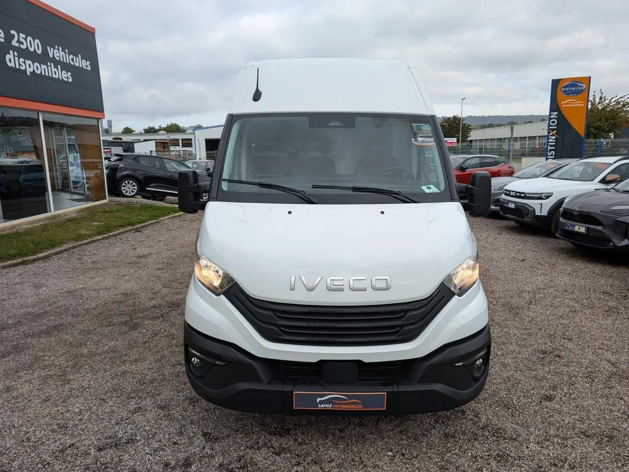 Vue avant d'un utilitaire Iveco Daily blanc avec calandre noire et phares allumés sur un parking.