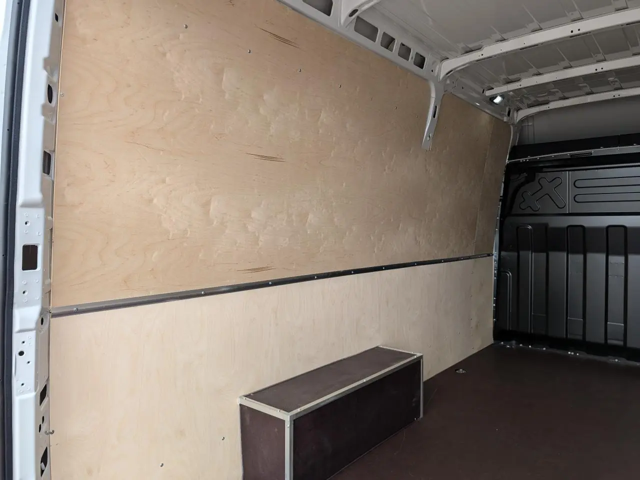 Vue intérieure côté gauche du coffre du fourgon blanc Iveco Daily 35S16 avec habillage bois et plancher noir antidérapant.