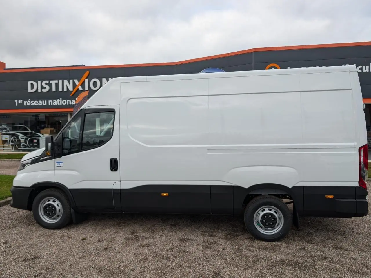 IVECO Daily blanc en vue de profil côté gauche, avec bas de caisse noir et porte coulissante sans fenêtre.