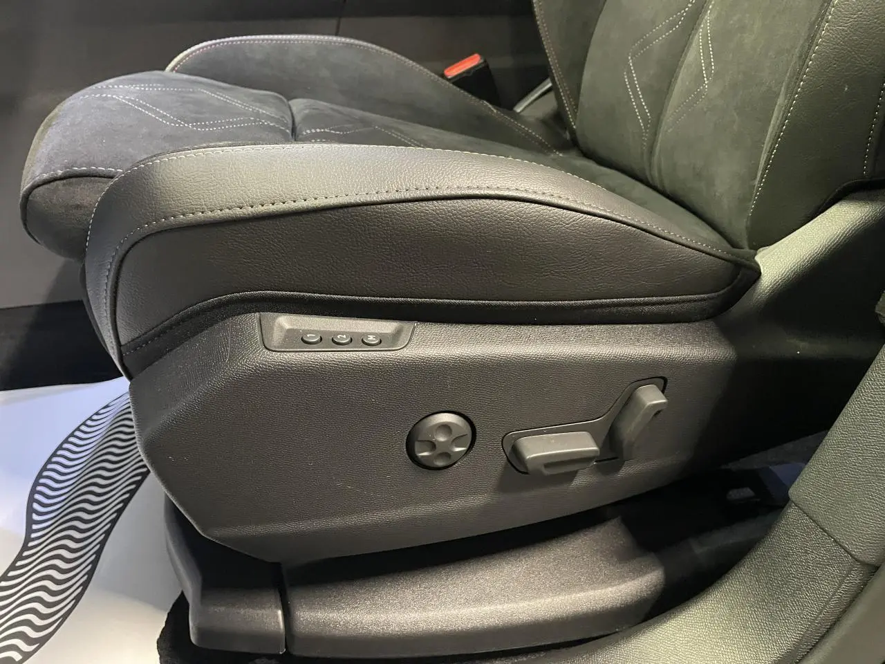 Détail du siège avant conducteur en Alcantara noir profond avec commandes électriques sur le côté gauche.