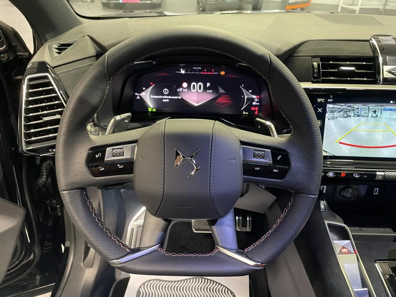 Vue intérieure centrée sur le volant DS en cuir noir perforé avec surpiqûres rouges et tableau de bord numérique allumé.