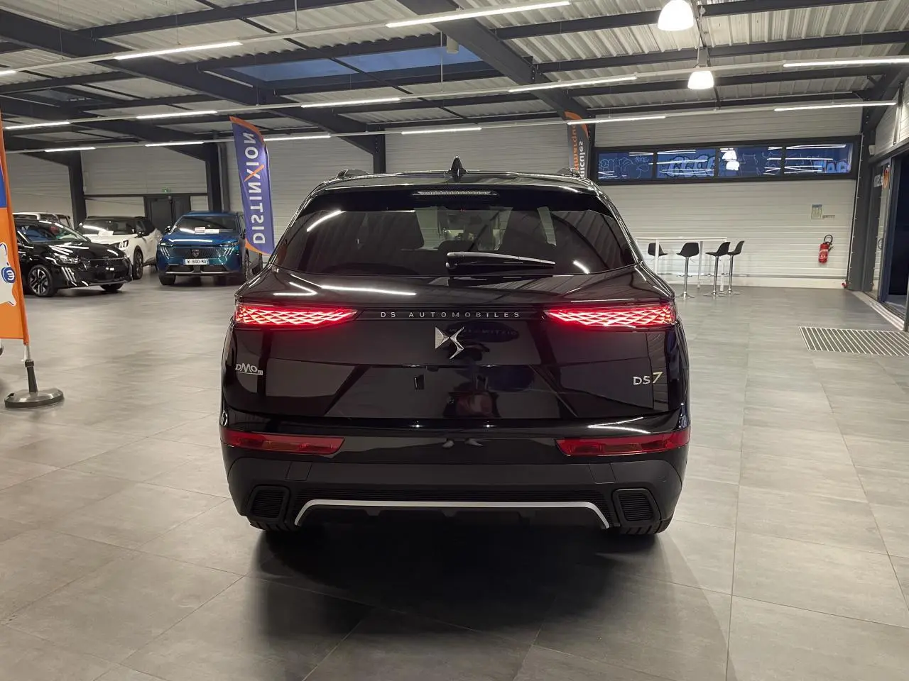Vue arrière d'un DS7 Crossback noir métallisé avec feux arrière LED 3D allumés dans un showroom.