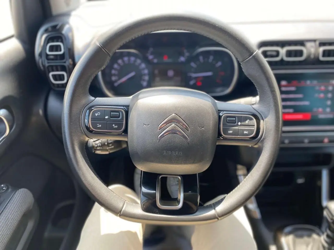Vue rapprochée du volant noir de la Citroën C3 Aircross 2023, avec commandes intégrées et tableau de bord flou en arrière-plan.