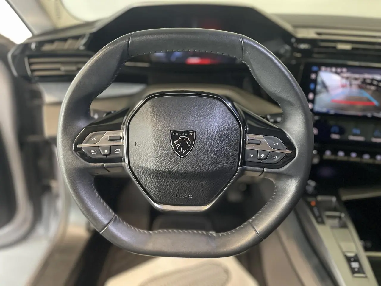 Volant en cuir noir de la Peugeot 308 2022 avec commandes intégrées et écran tactile affichant la caméra de recul.