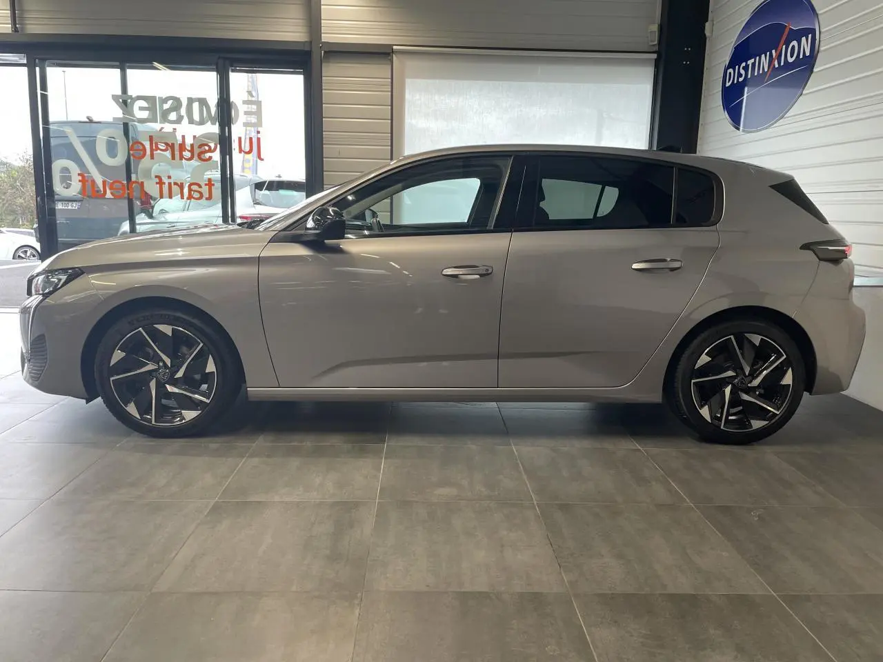 Profil côté gauche de la Peugeot 308 gris Artense 2022 avec jantes alliage 17'' et vitres surteintées en showroom.