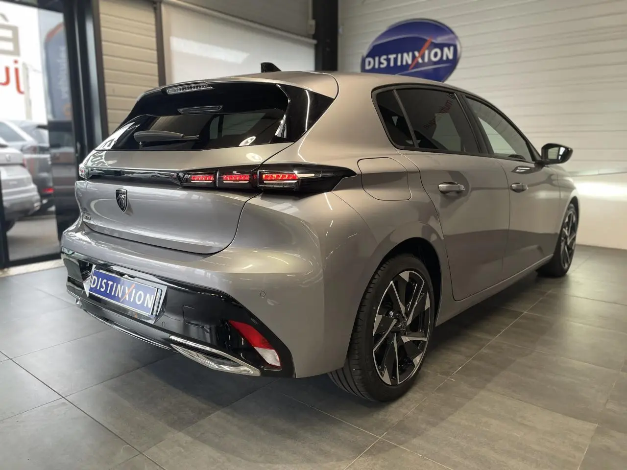 Vue 3/4 arrière droit d'une Peugeot 308 gris Artense avec feux arrière LED et jantes alliage 17 pouces en showroom.