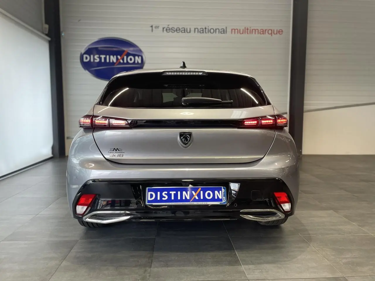Vue arrière d'une Peugeot 308 gris Artense avec feux LED allumés et double sortie d'échappement chromée dans un showroom.