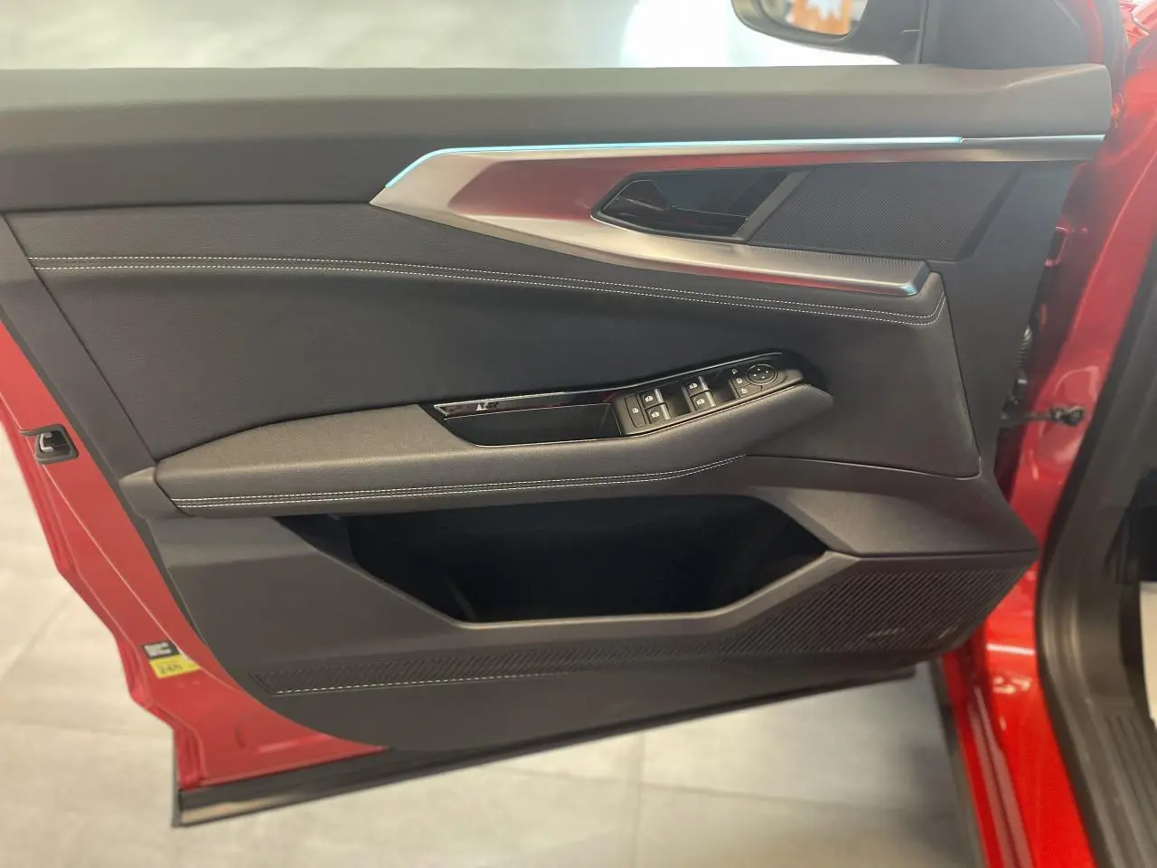 Porte avant gauche ouverte de la Renault Rafale rouge, montrant les commandes de vitres et le revêtement textile noir avec surpiqûres blanches.