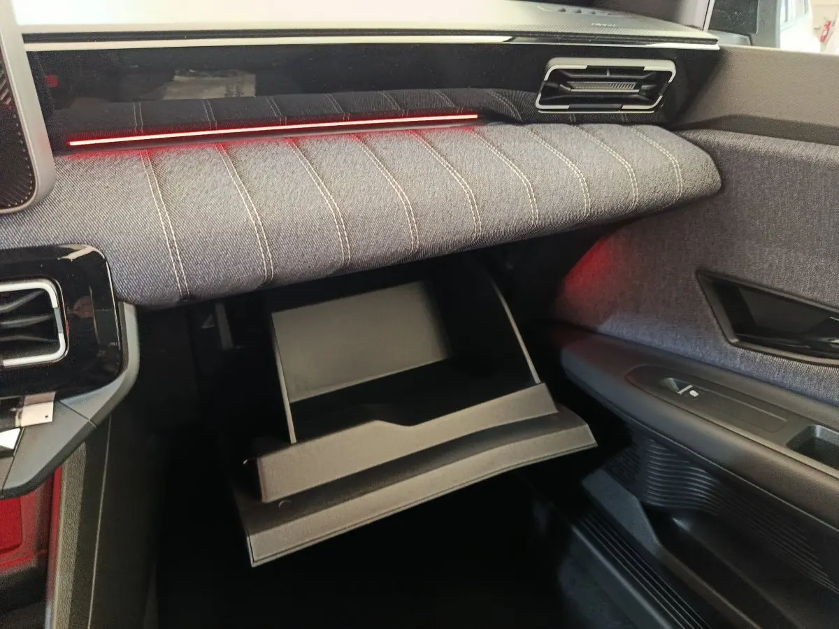Intérieur de la Renault R5 Techno 150 ch 2025, vue côté passager sur la boîte à gants ouverte et tissu gris avec éclairage rouge.