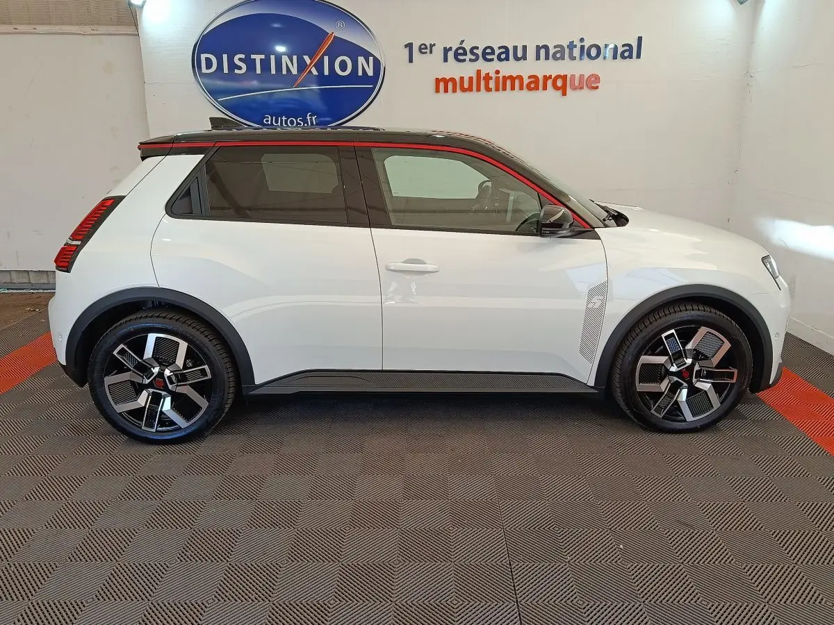 Vue de profil côté gauche d'une Renault R5 Techno électrique blanche avec toit noir et jantes stylisées en concession.