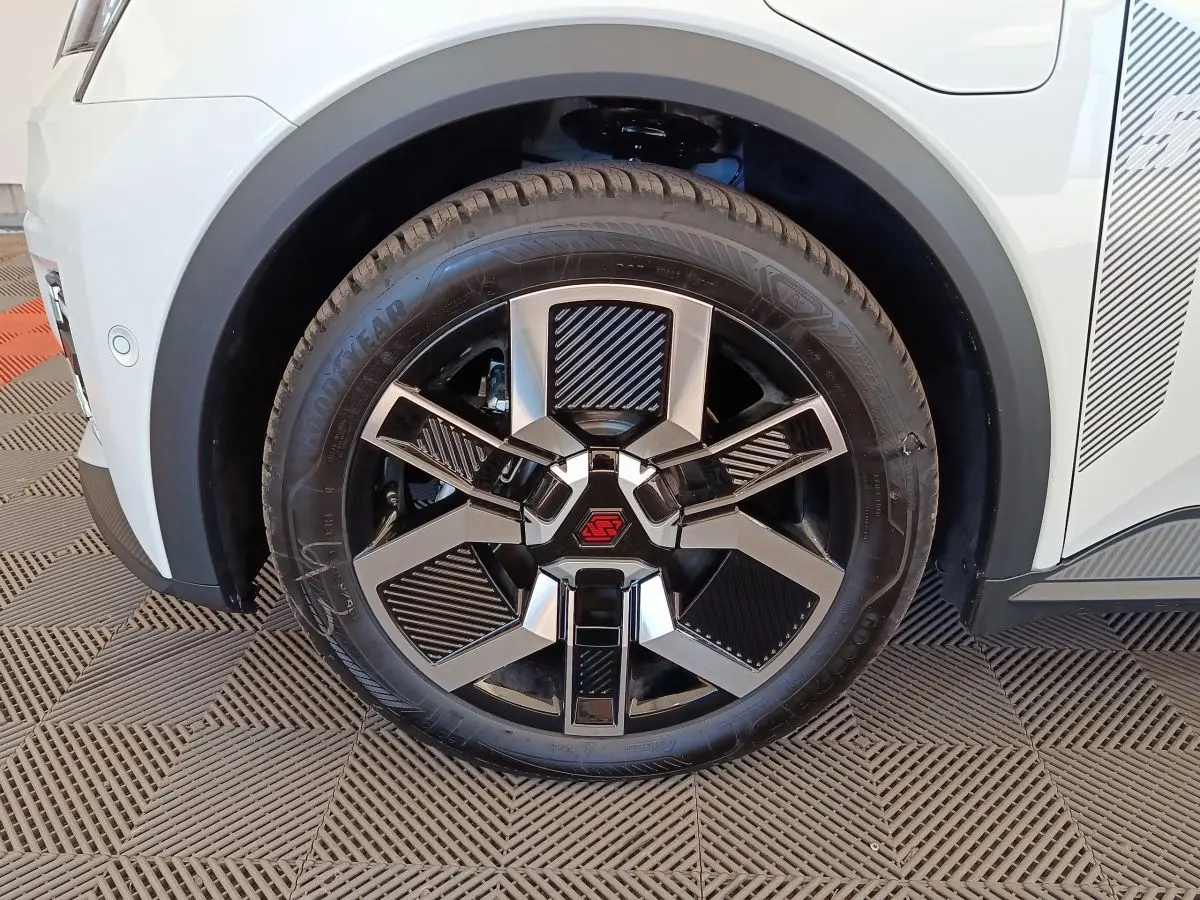 Gros plan sur la roue avant gauche de la Renault R5 Techno blanche, avec jante noire et argent au design géométrique.