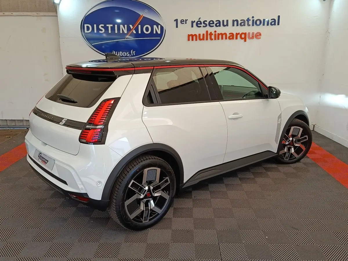 Vue 3/4 arrière droite d'une Renault R5 Techno blanche avec toit noir et jantes noires à motifs géométriques.