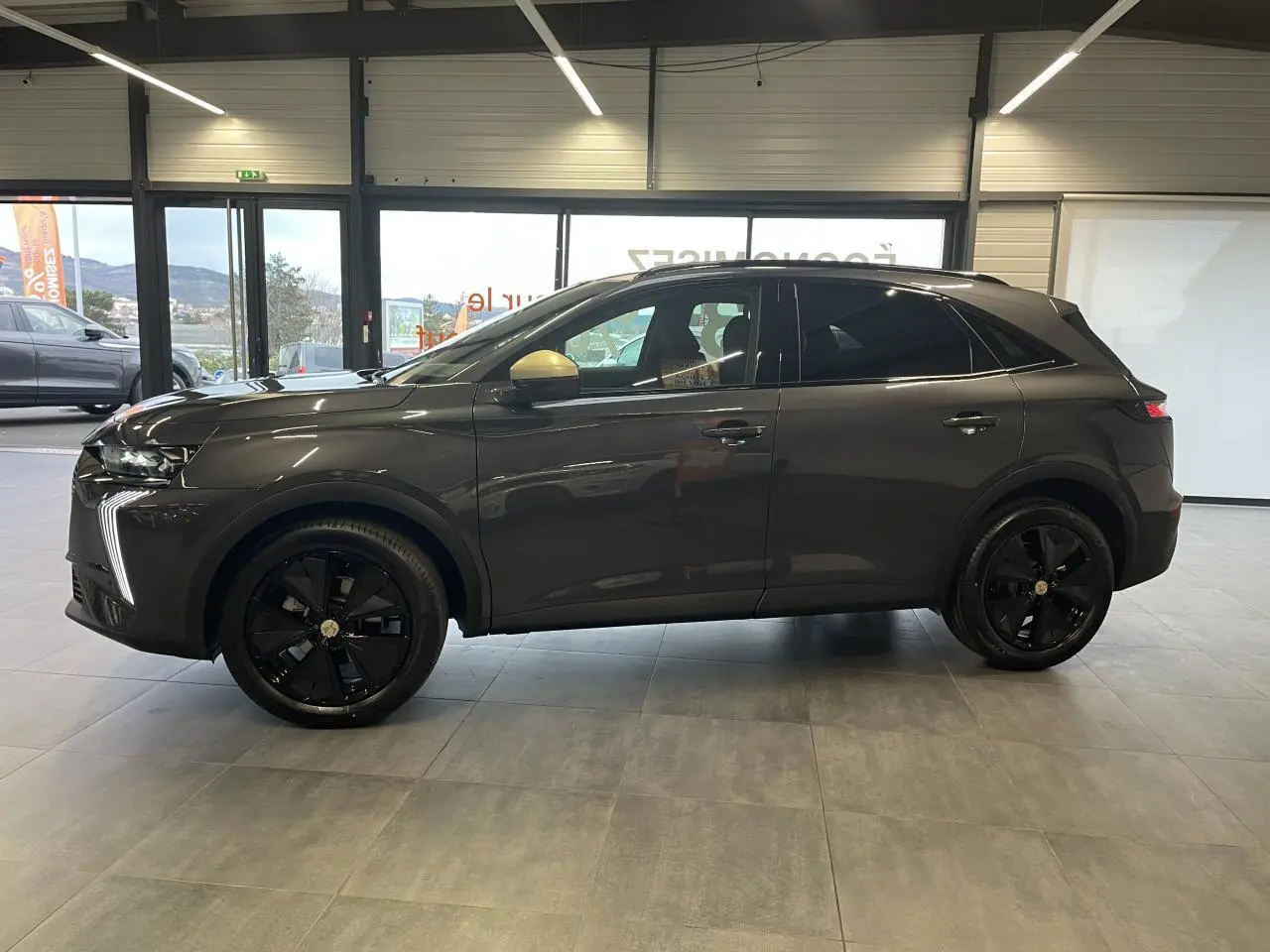 Vue latérale droite du DS7 Crossback gris titanium avec jantes noires et rétroviseurs dorés satinés en intérieur showroom.