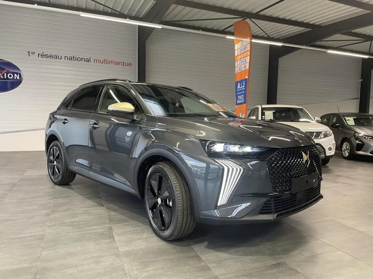 Vue 3/4 avant du DS7 Crossback gris titanium avec calandre noire et coques de rétroviseurs dorées satinées en showroom.