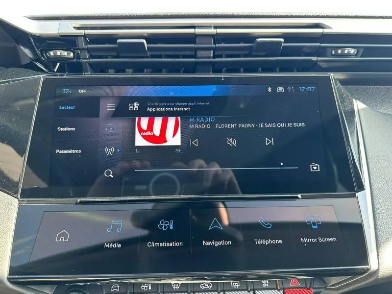 Vue rapprochée de l'écran tactile central noir du tableau de bord de la Peugeot 308 2025, affichant la radio et les commandes multimédia.