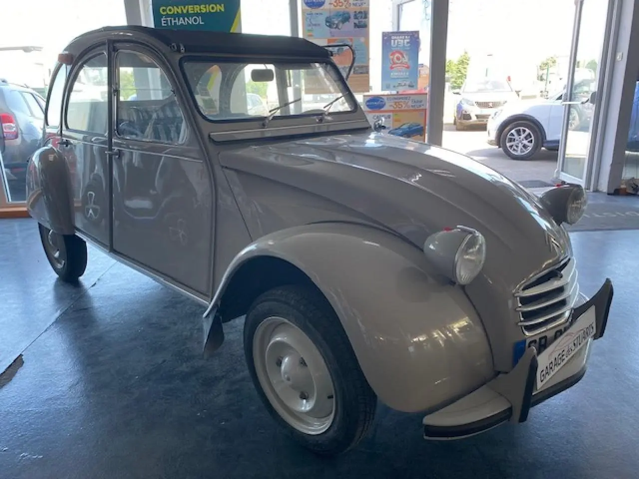 Citroën 2 CV beige clair refaite à neuf vue 3/4 avant gauche dans un garage lumineux.