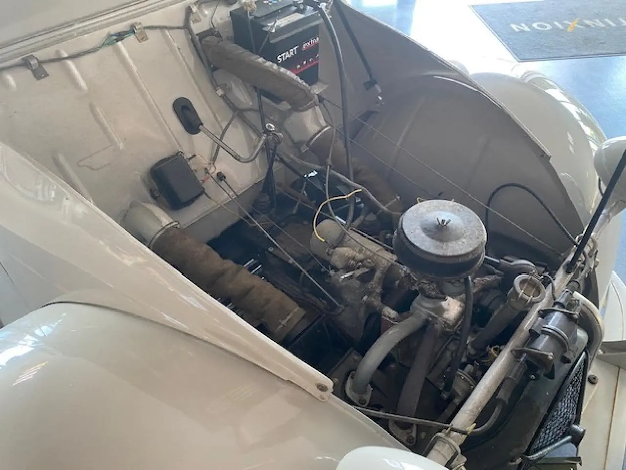 Moteur visible sous le capot ouvert d'une Citroën 2 CV beige clair refaite à neuf, vue de trois quarts avant droit.