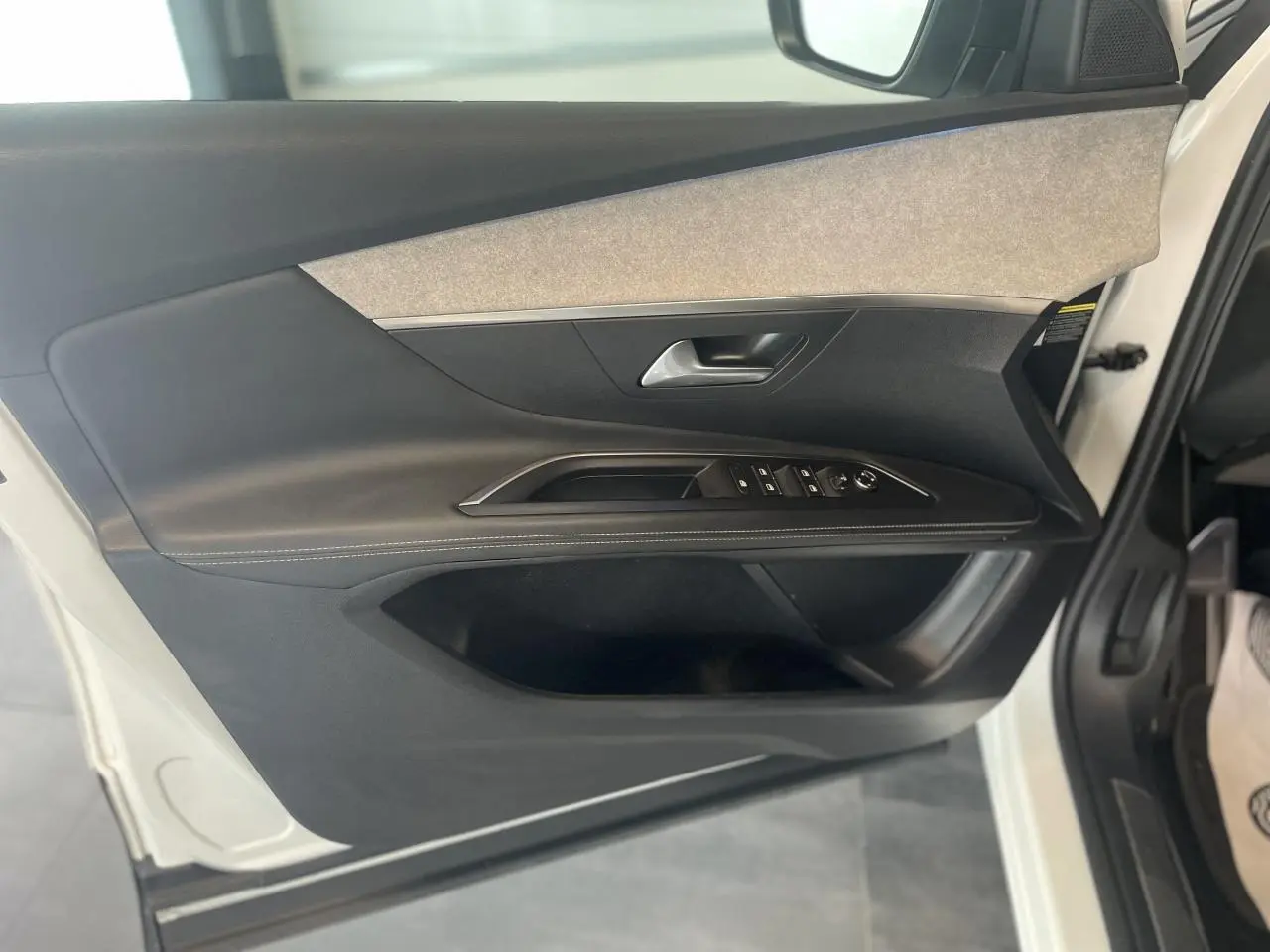 Porte avant gauche ouverte d'un Peugeot 3008 blanc nacré, montrant garniture noire et grise avec commandes électriques.