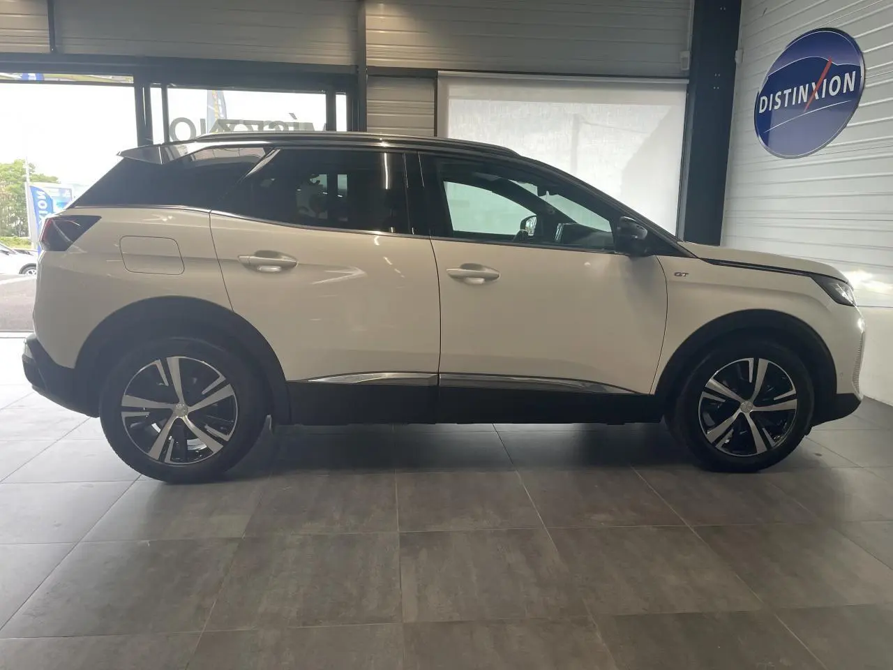 Profil droit du Peugeot 3008 GT blanc nacré avec toit noir et jantes alliage bi-ton dans un showroom.