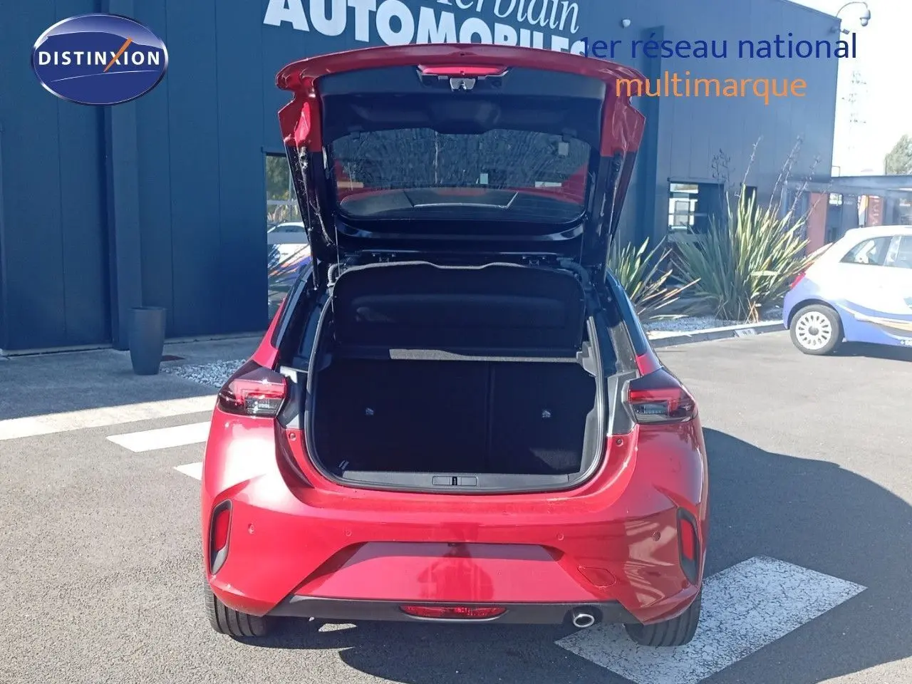 Vue arrière d'une Opel Corsa rouge Kardio métal avec toit noir, coffre ouvert sur un parking extérieur.