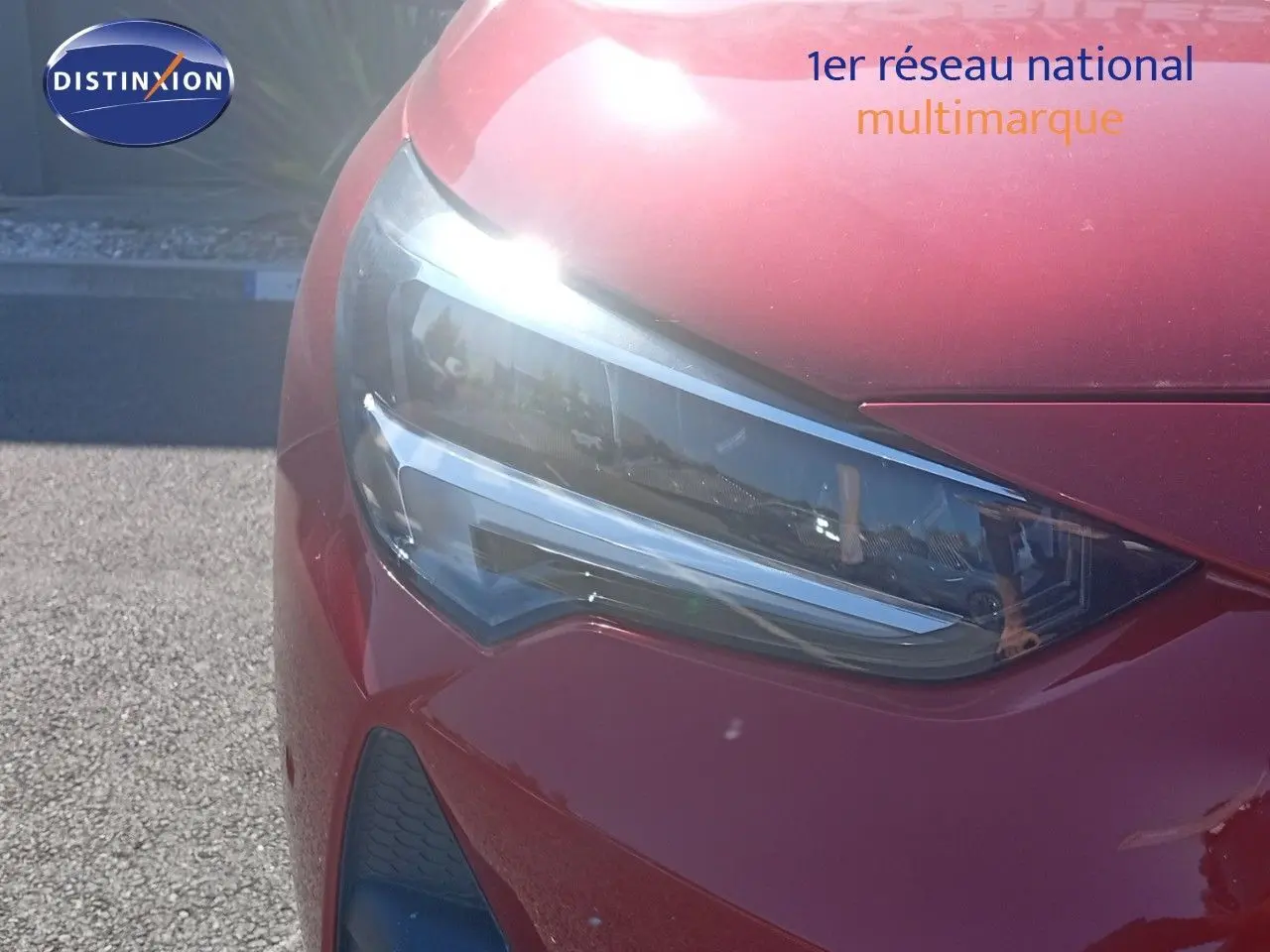 Gros plan sur le phare avant gauche d'une Opel Corsa rouge Kardio métal avec toit noir, 2023, sous lumière naturelle.