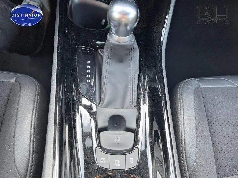 Gros plan sur la console centrale noire brillante du Toyota C-HR blanc nacré, avec levier de vitesse automatique et sièges gris.