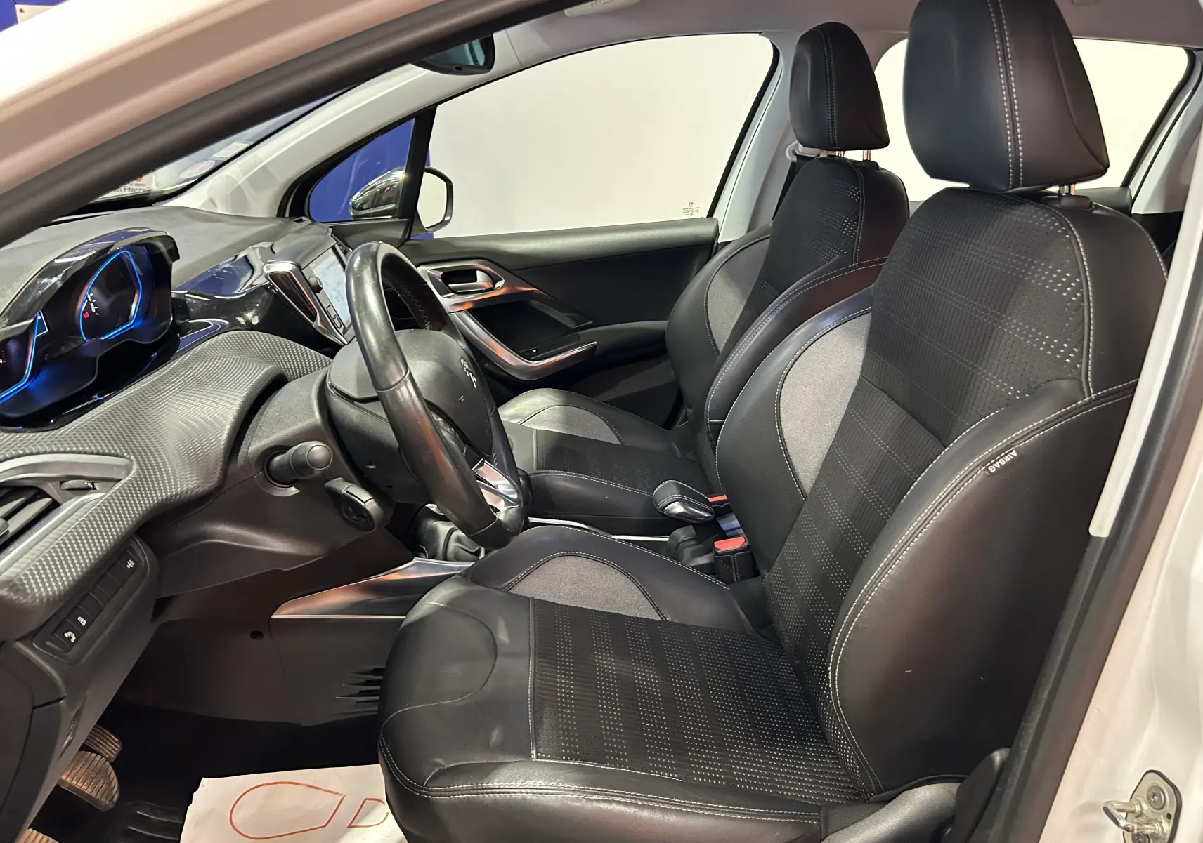 Intérieur avant du Peugeot 2008 blanc, vue côté gauche, sièges cuir noirs avec coutures blanches et tableau de bord moderne.