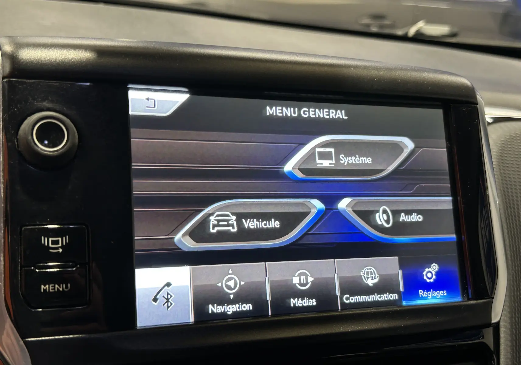 Écran tactile central du tableau de bord du Peugeot 2008 blanc, affichant le menu général avec options système, véhicule et audio.