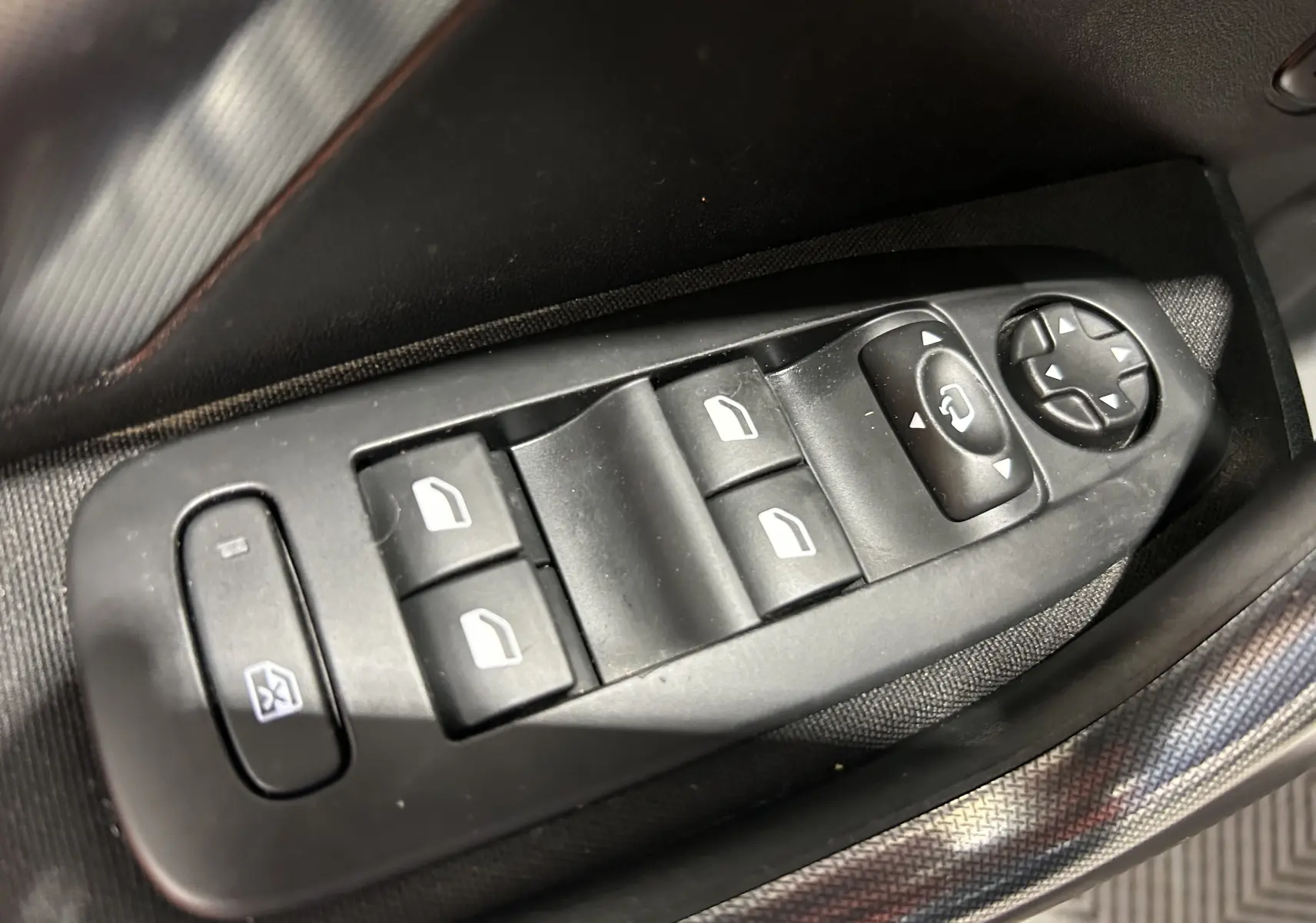 Gros plan sur les commandes des vitres électriques et rétroviseurs côté conducteur d'un Peugeot 2008 blanc de 2014.