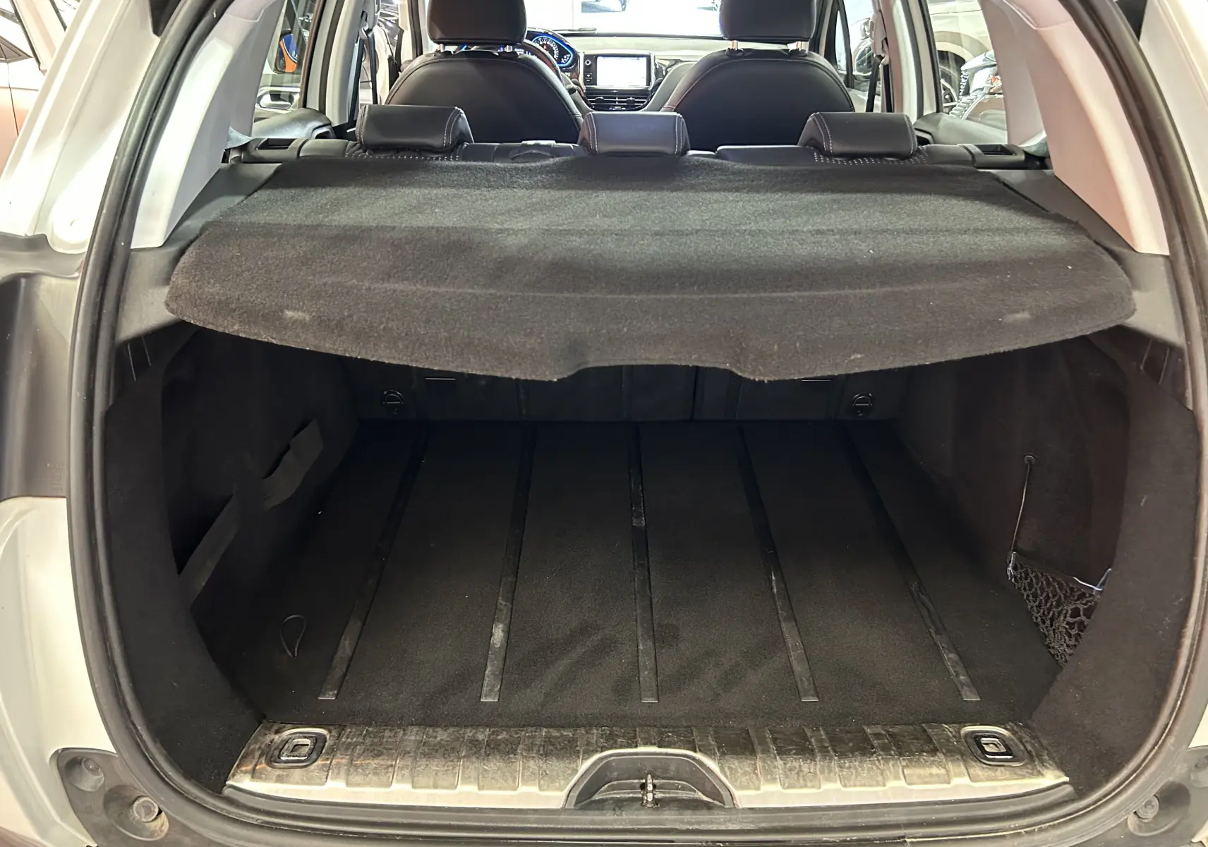 Coffre ouvert d’un Peugeot 2008 blanc, vue arrière montrant l’espace de chargement et la tablette cache-bagages.