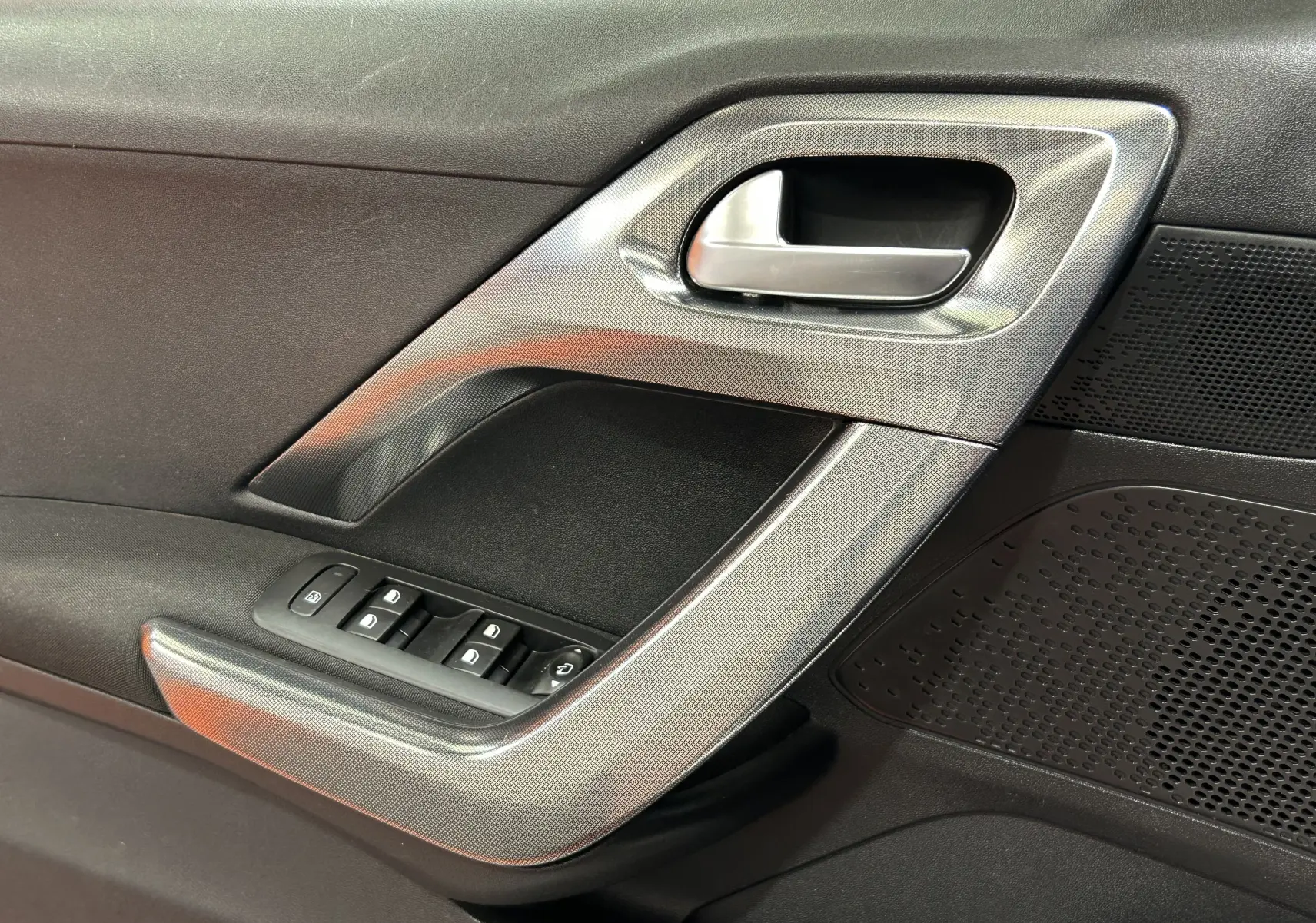 Vue rapprochée de la poignée intérieure côté gauche de la porte avant d'une Peugeot 2008 blanche, avec commandes de vitres.