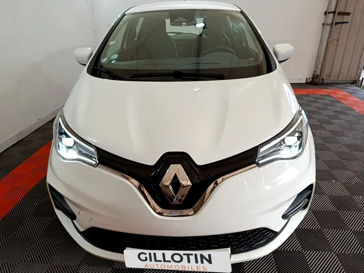 Vue avant d'une Renault ZOE Business R110 blanche avec phares LED allumés dans un garage.
