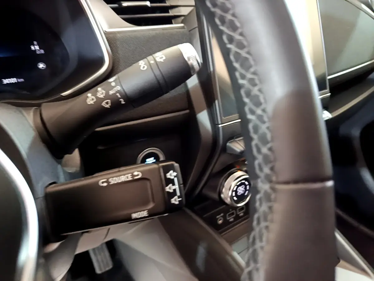 Gros plan sur la commande multifonction et le volant en cuir synthétique côté gauche du tableau de bord de la Renault ZOE blanche.