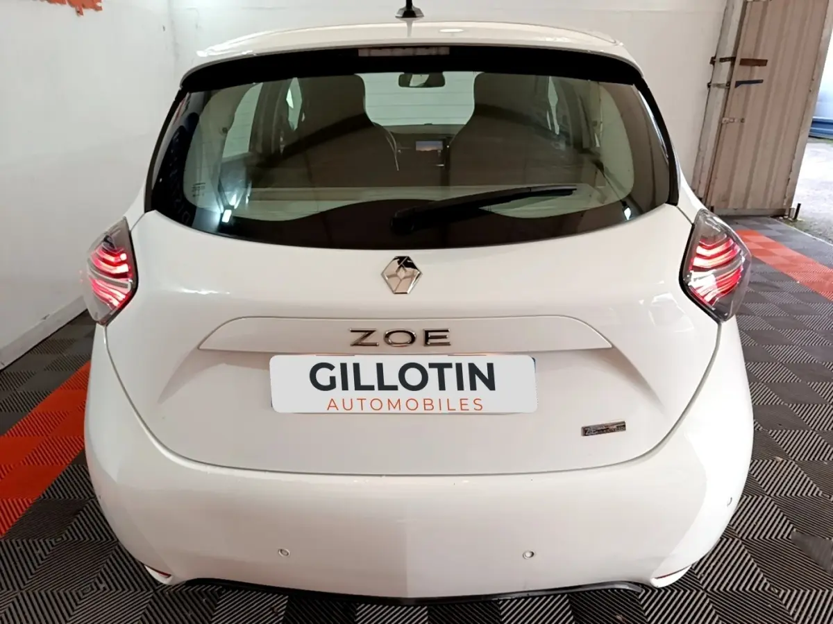 Vue arrière d'une Renault ZOE blanche 2021 avec feux LED allumés et logo ZOE bien visible.