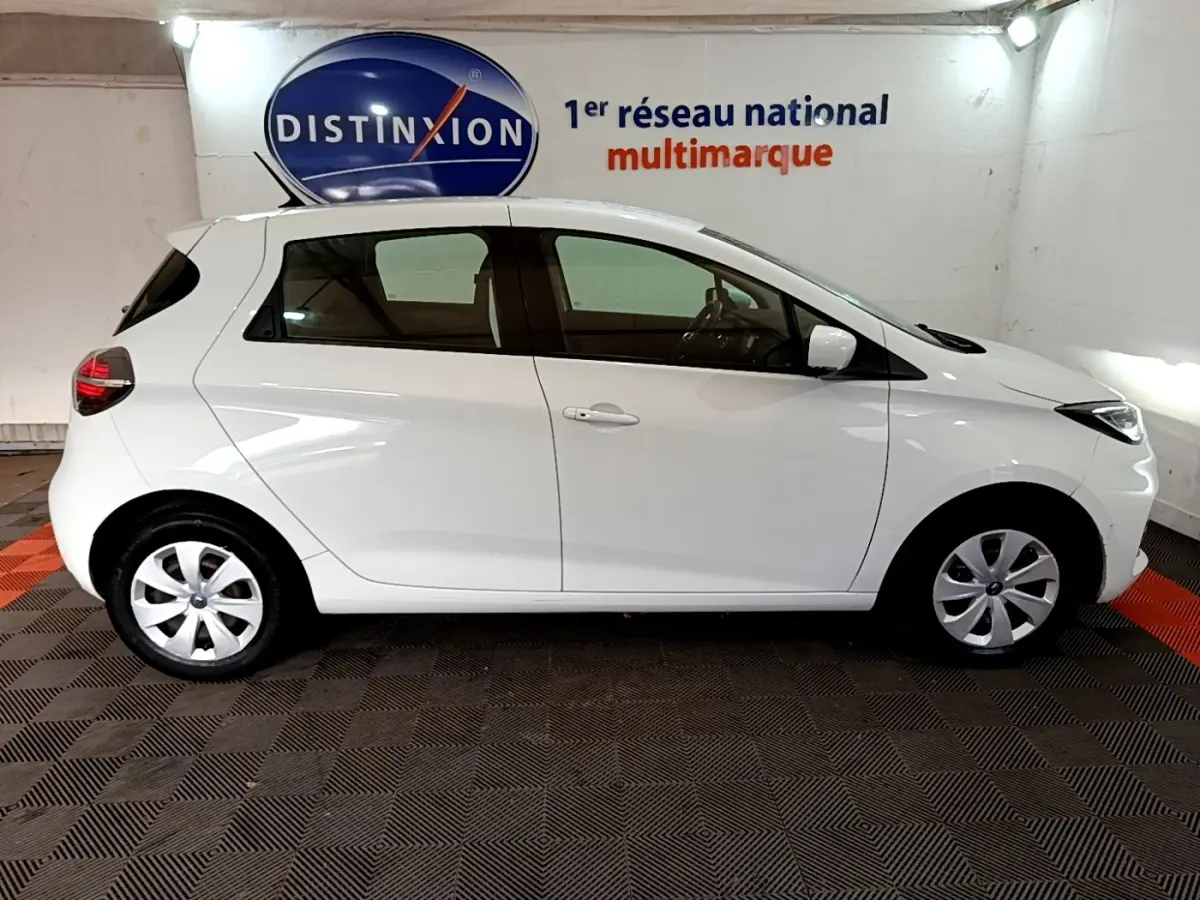 Profil droit d'une Renault ZOE Business R110 blanche de 2021, compacte et électrique, en intérieur sur sol damier noir et rouge.