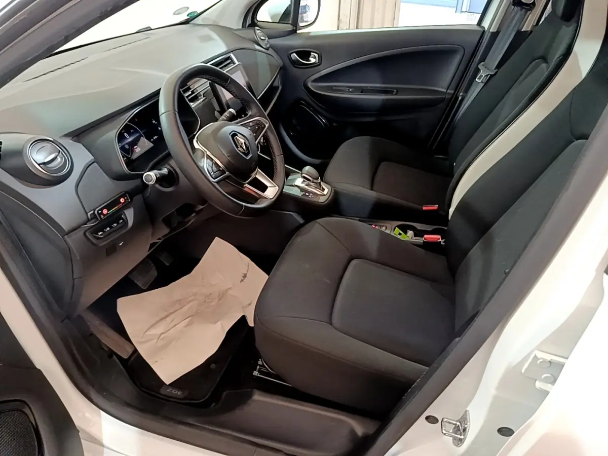 Vue intérieure côté conducteur de la Renault ZOE Business R110 blanc, avec volant multifonctions et sièges noirs.
