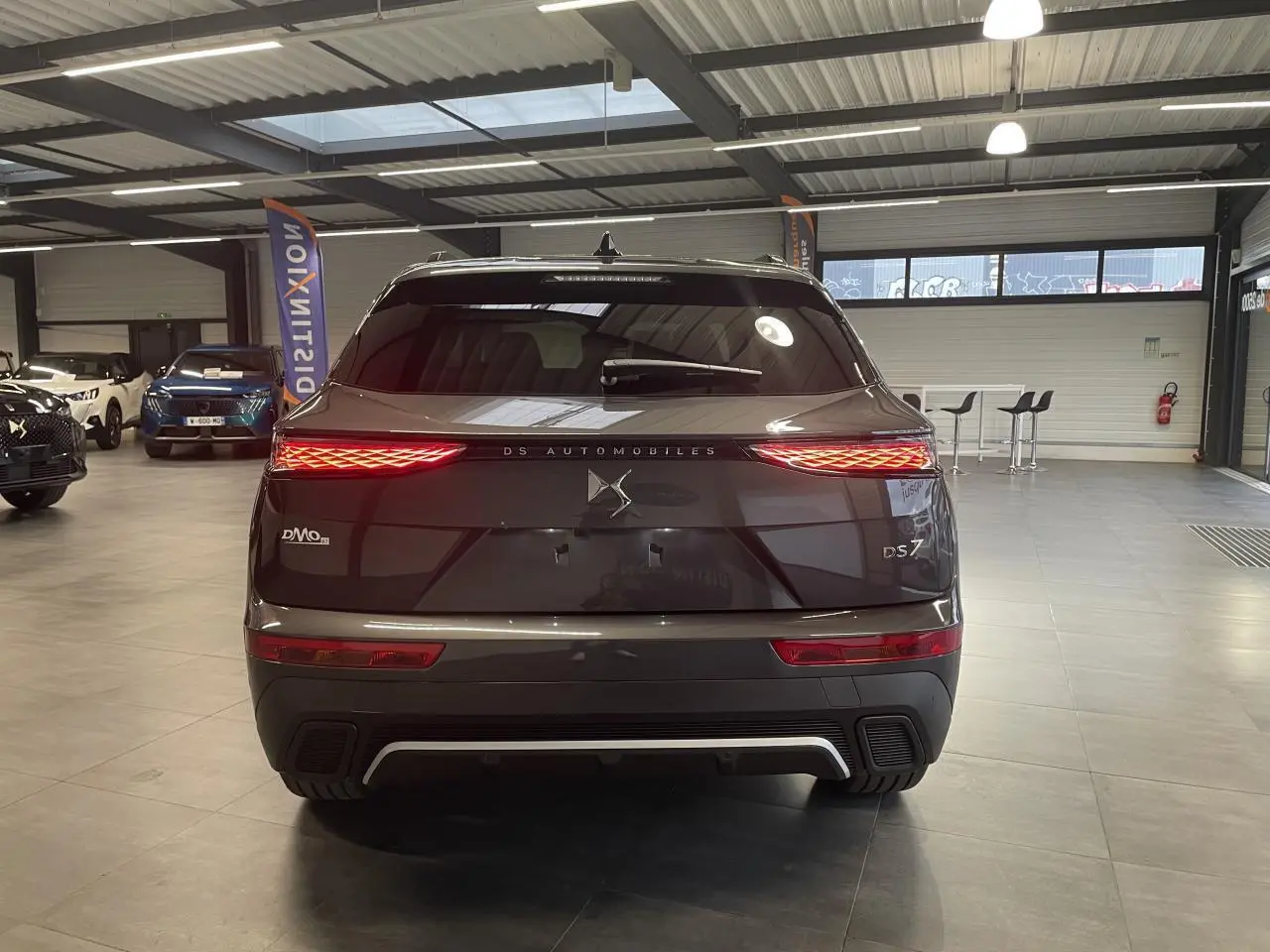 Vue arrière d'un DS7 Crossback gris titanium avec feux arrière LED allumés et logo DS Automobiles au centre.