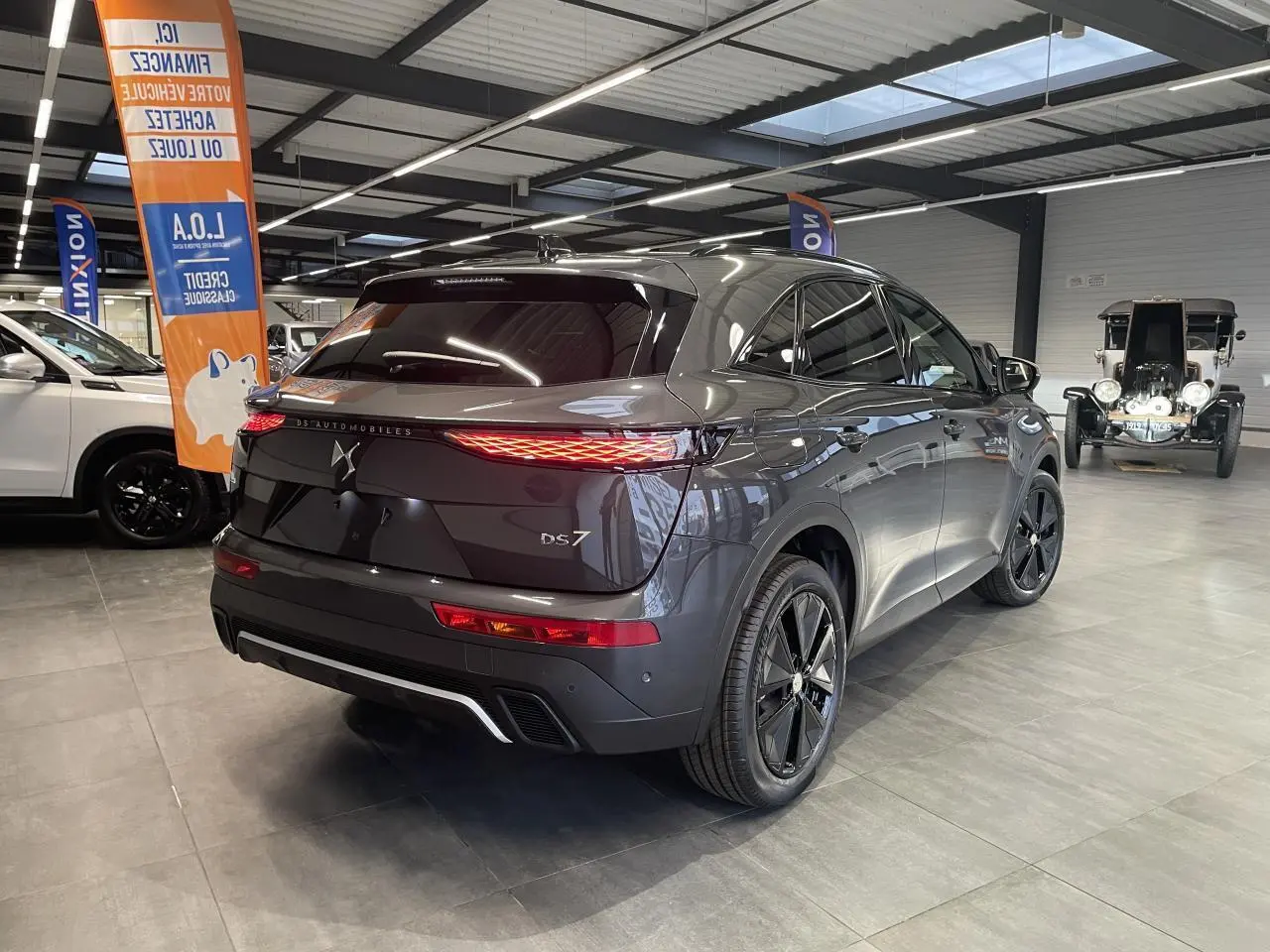 Vue 3/4 arrière droite du DS7 Crossback gris titanium avec feux arrière LED et jantes noires en showroom.
