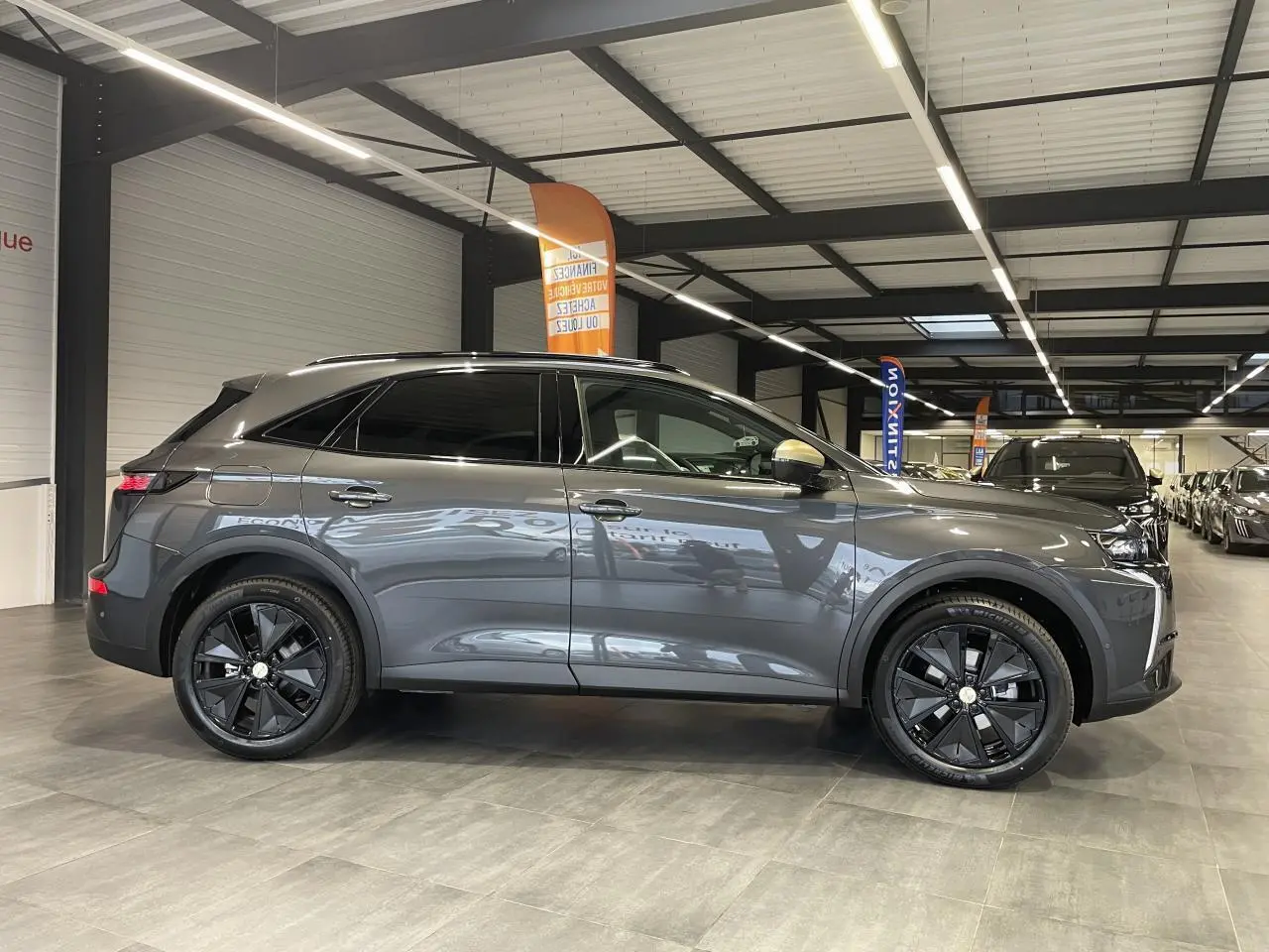 Vue de profil côté gauche du DS7 Crossback gris titanium, avec jantes alliage noires et vitres teintées, en intérieur showroom.